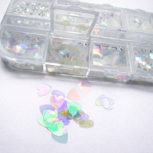 Ask med 12 tunna, transparenta paljetter i mixade former och storlekar. Skiftande finish, enkla att forma mot nageln och perfekt