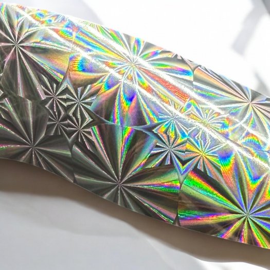 Ett holografiskt nagelfolie med ett geometriskt mönster som skapar ett färgsprakande regnbågsspektrum när ljuset träffar ytan. P